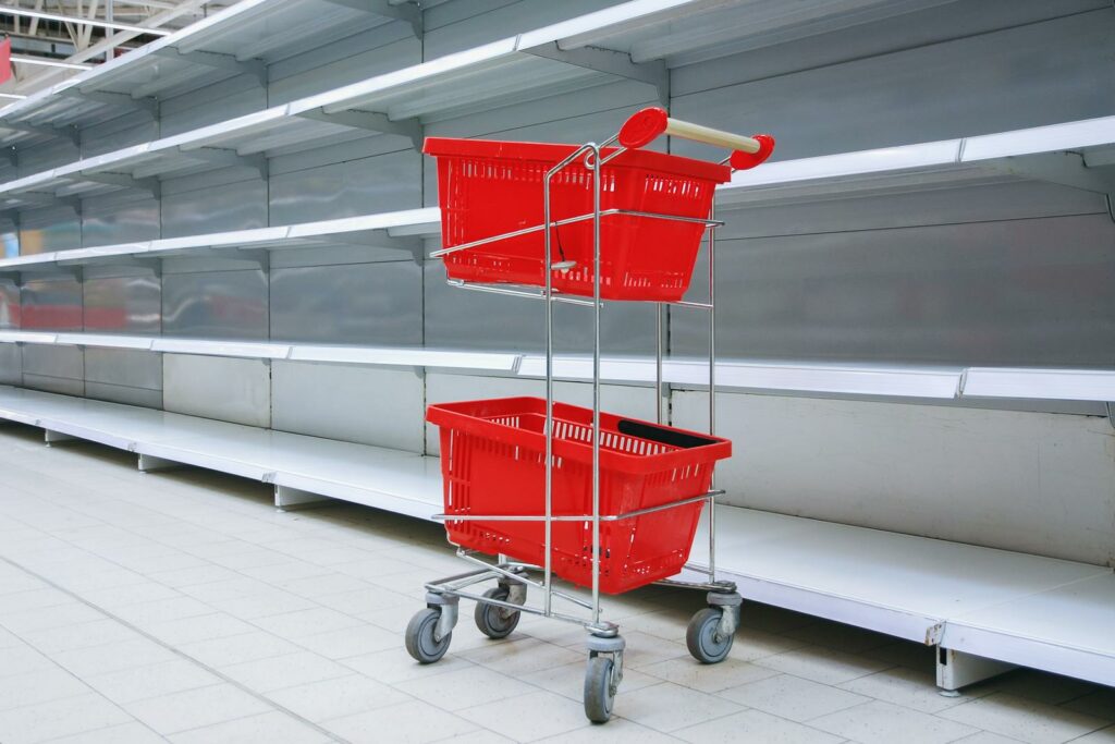 Shopping trolley with empty baskets against empty shelves in grocery store